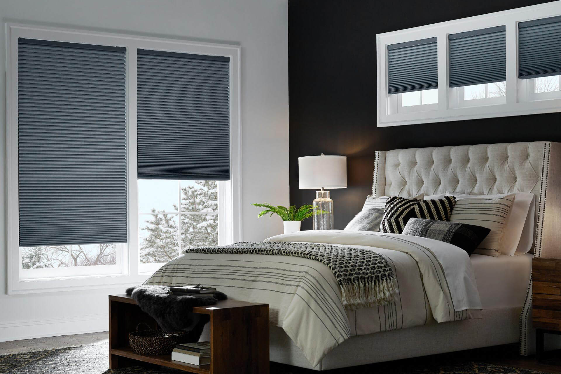 A black and white painted bedroom with dark blue honeycomb shades on two large windows and three smaller windows above the bed.
