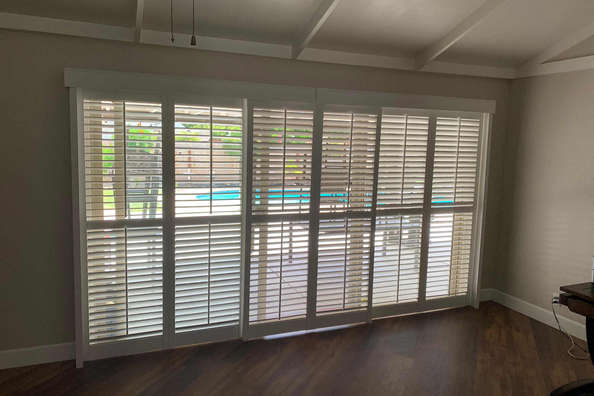 A long wall of glass doors that lead to a backyard pool covered with shutters.