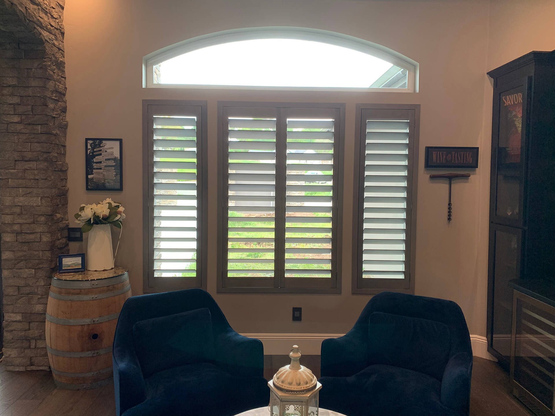 A winery themed seating area with shutters covering the windows behind two blue chairs.