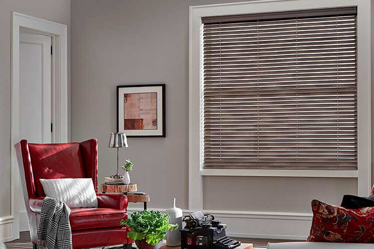 A living room with a red chair that has brown blinds covering a window.