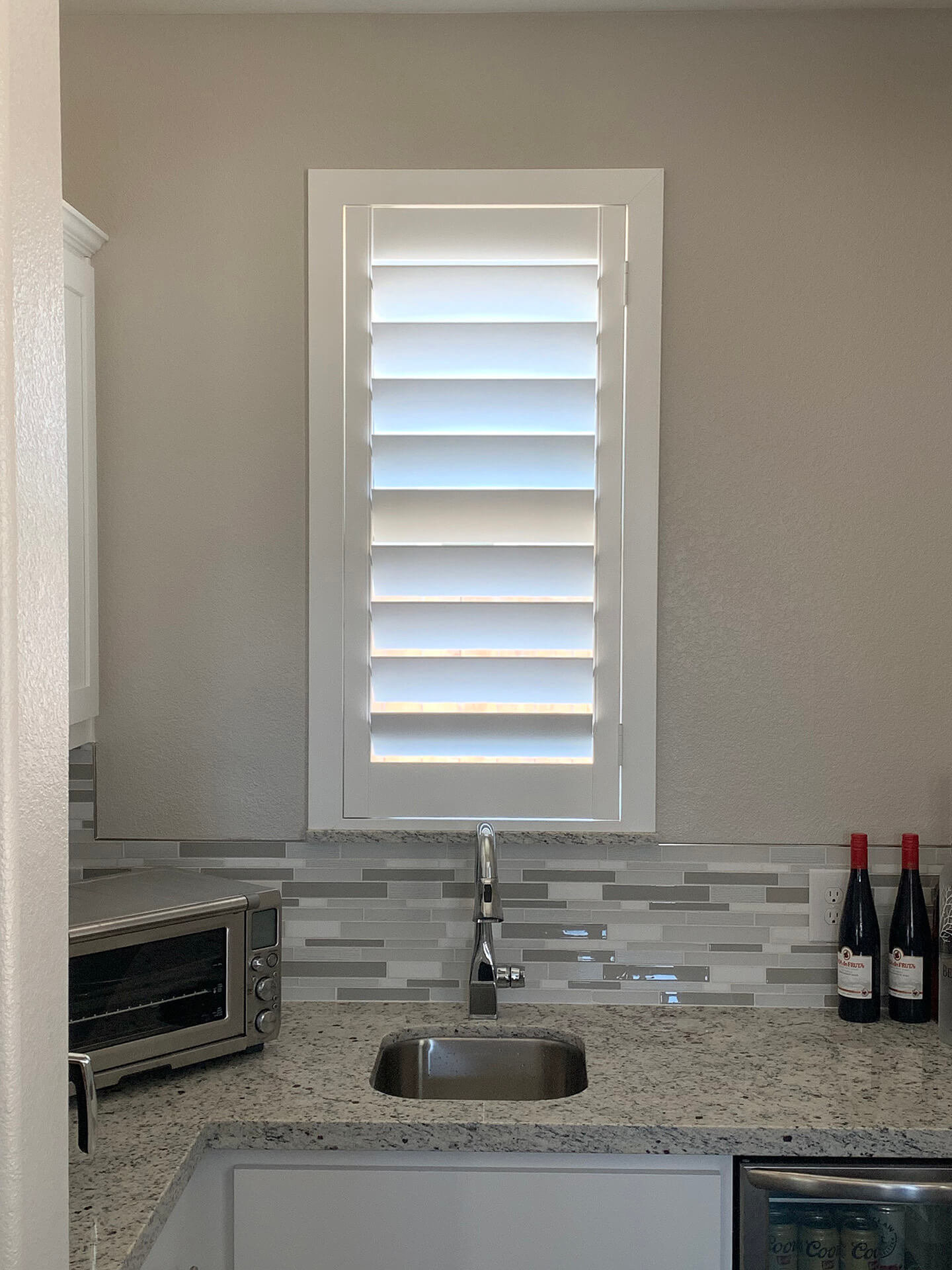 A small window shutter over a small kitchen window with a small kitchen sink.